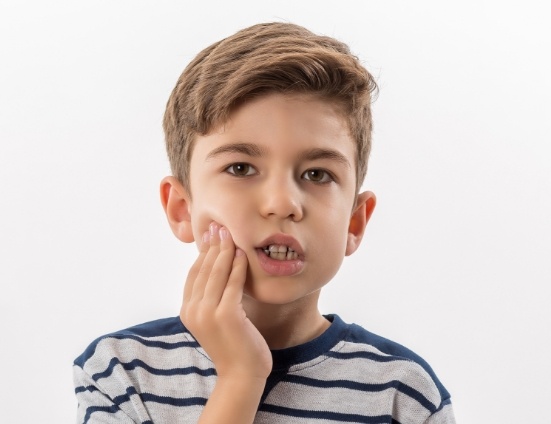 Young boy touching his cheek in pain