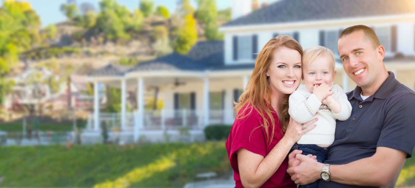 Man and woman smiling and holding their baby in their front yard